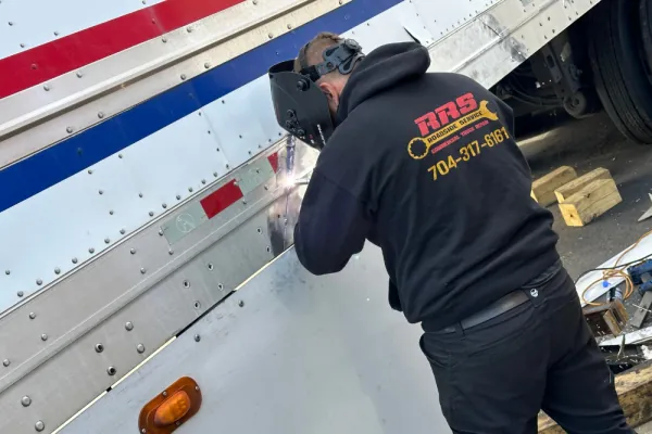 Technician welding a truck trailer panel during a mobile repair Technician welding a truck trailer panel during a mobile repair